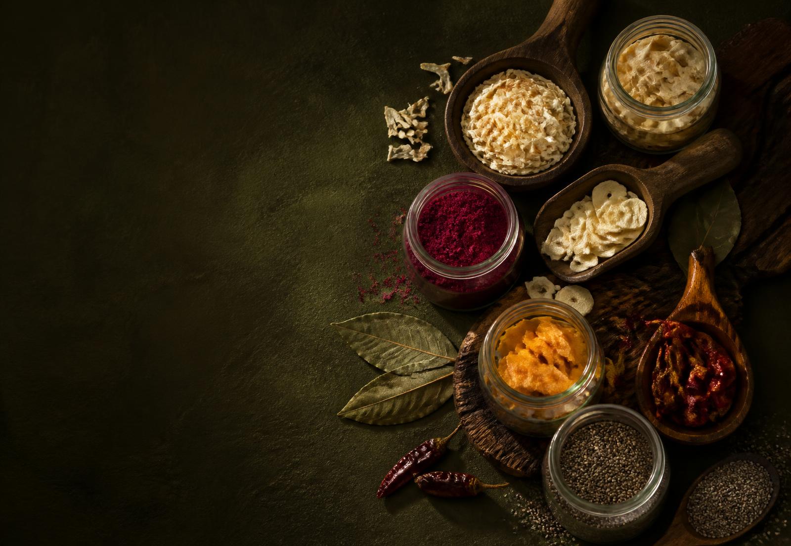 Dehydrated vegetables, fruits and seeds in jars on a dark olive surface